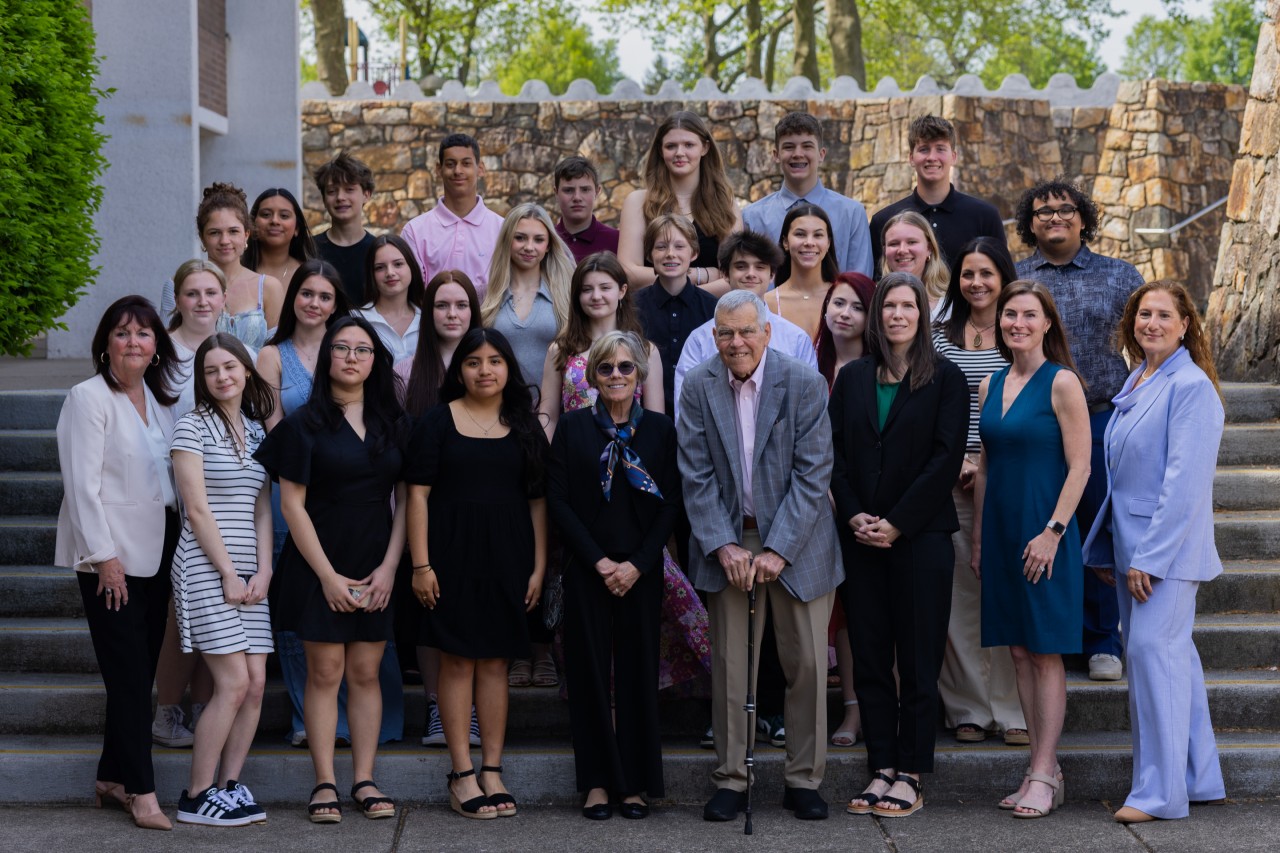 Group of people standing on outdoor steps in front of stone wall.